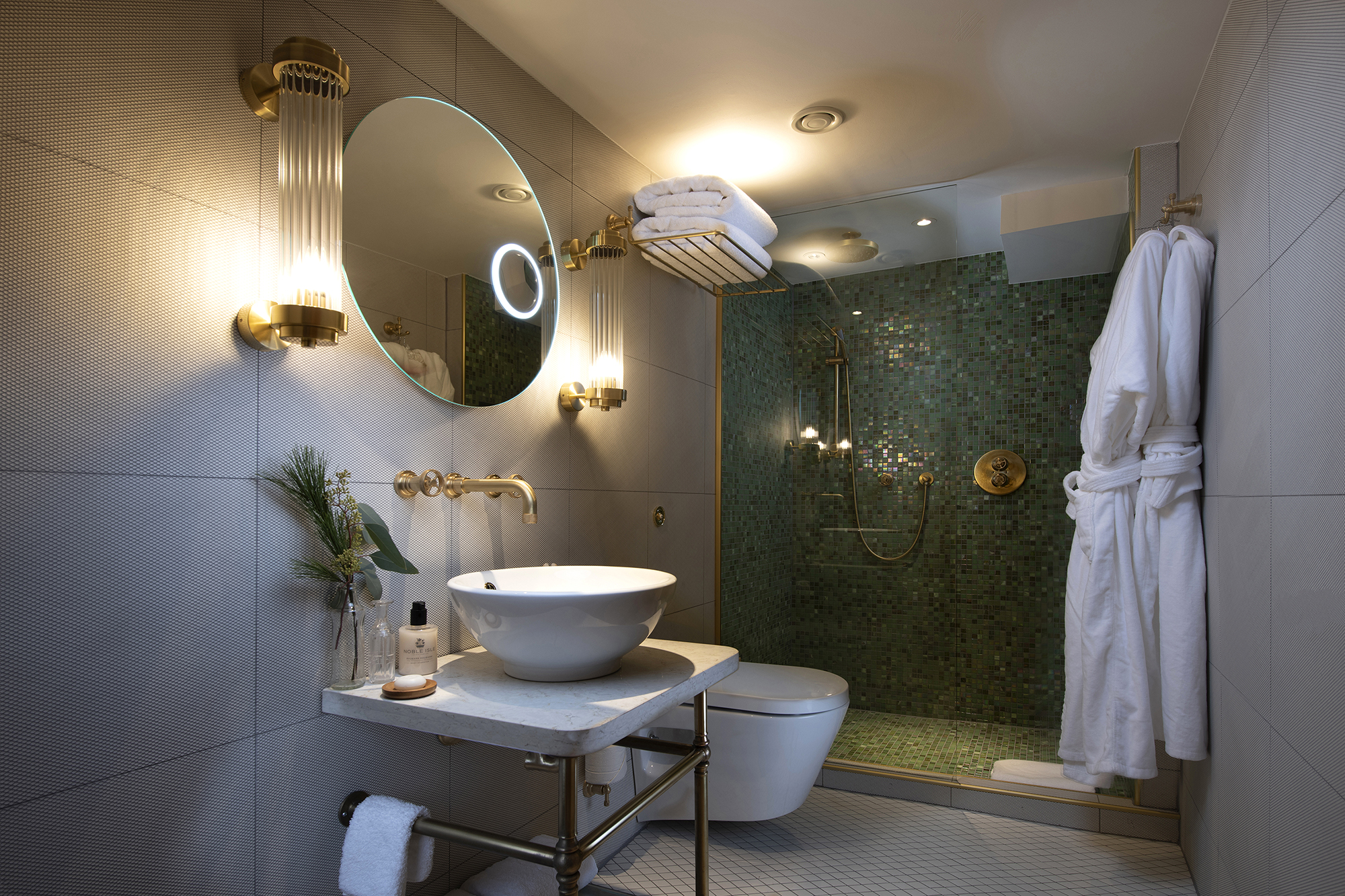 Elegant en-suite bathroom aboard Fingal, a luxury Edinburgh hotel, featuring a walk-in rainfall shower with green mosaic tiles, brass fittings, bespoke vanity, and plush bathrobes