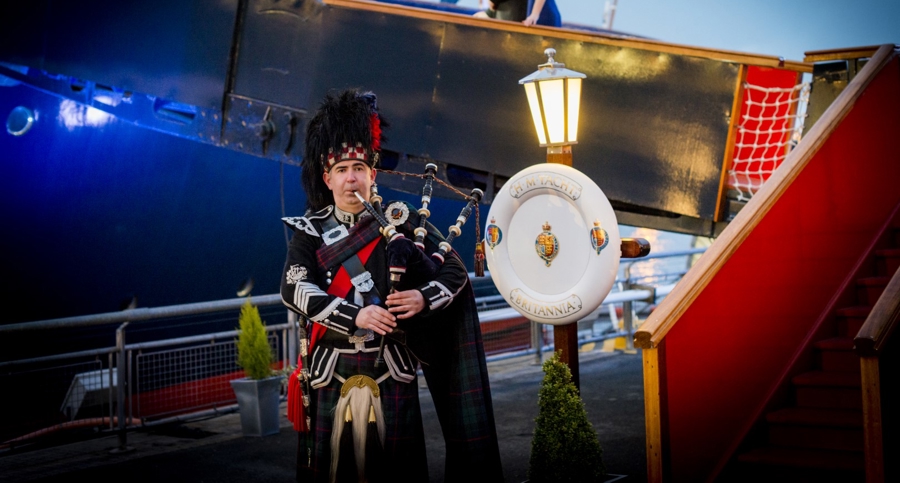 A piper is playing in front of the Royal Brow at The Royal Yacht Britannia.