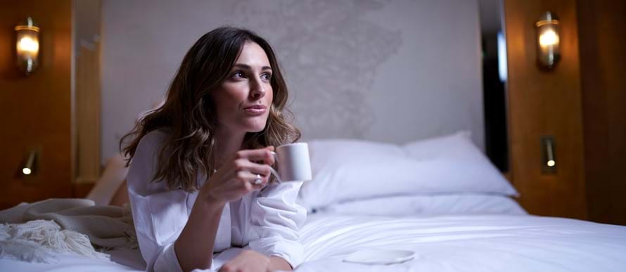 Woman in a white robe laying on a bed. 