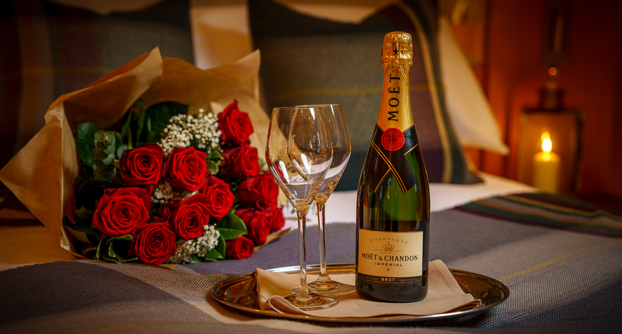 Bouquet of red roses and a bottle of Champagne on the bed