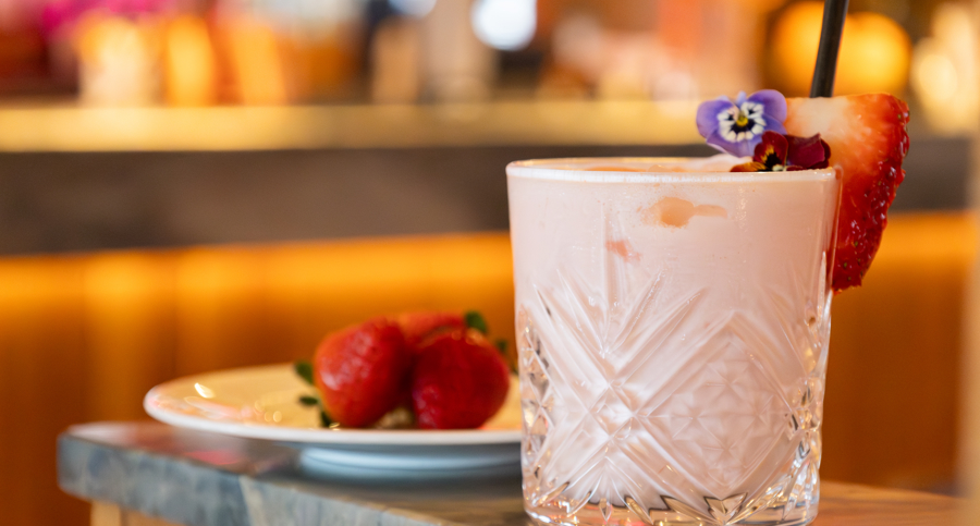 A pink cocktail garnished with a strawberry and pansy flowers. 