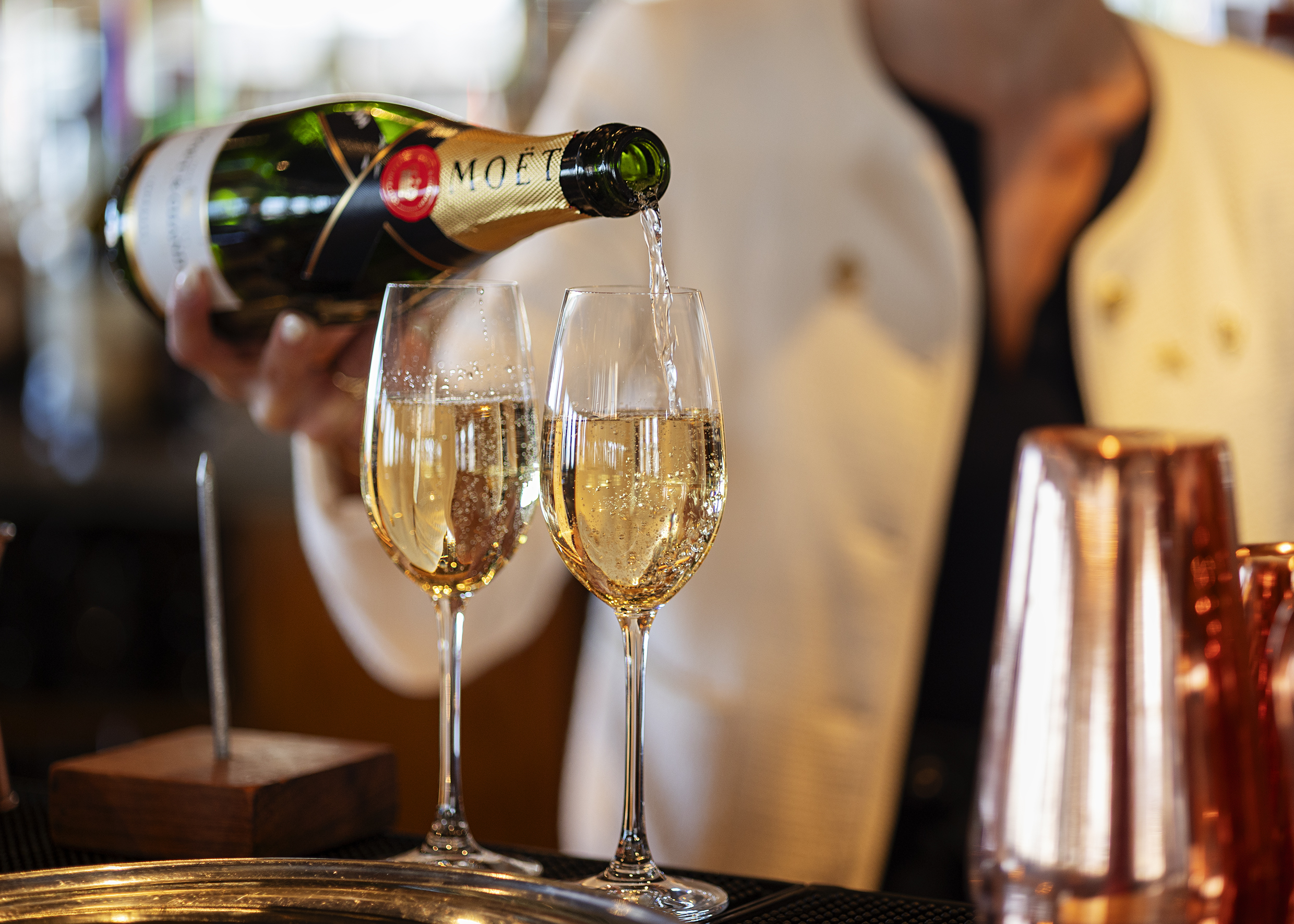 A hand pouring champagne into tow glasses on a table. During New Year and Hogmanay Event