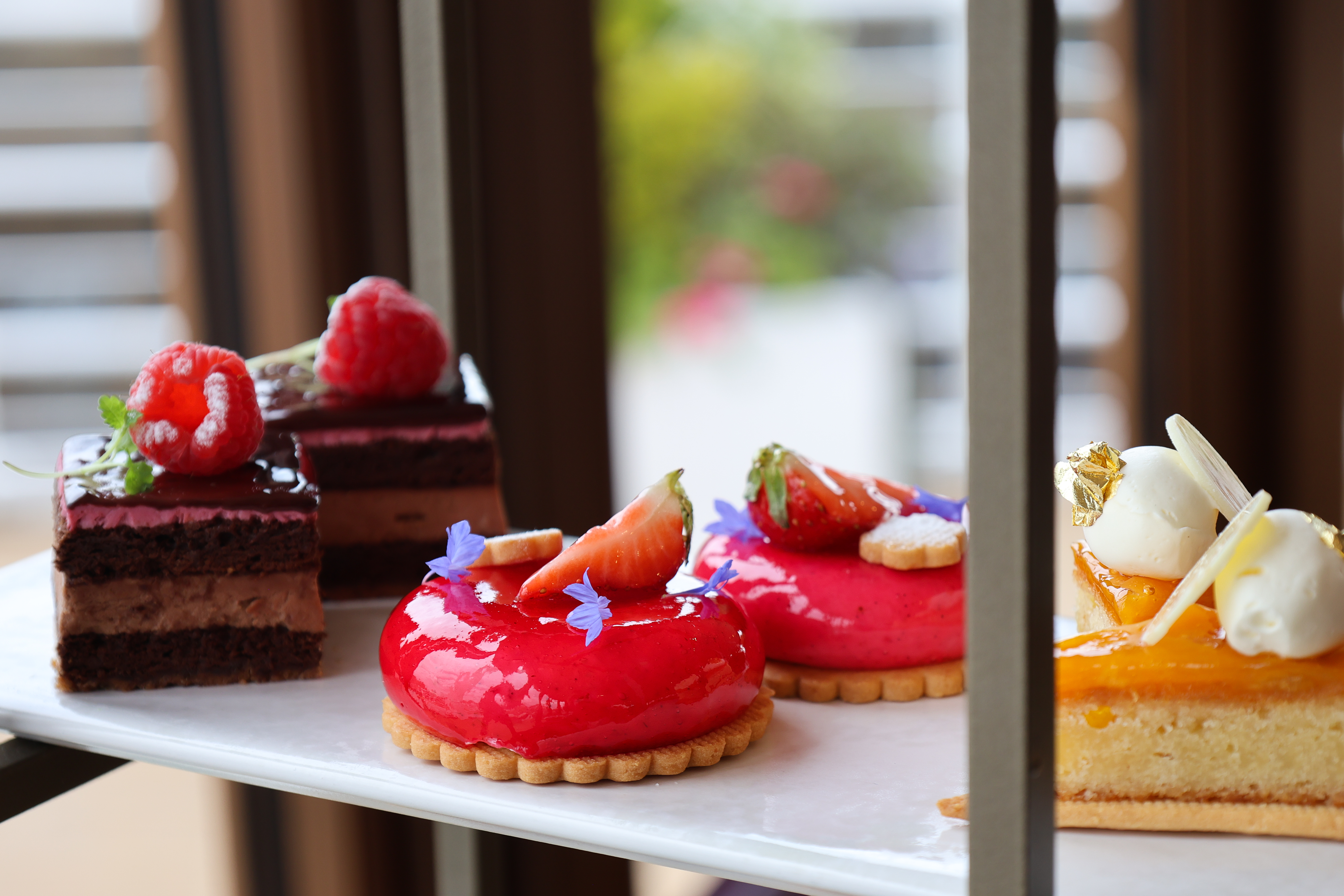 Marble tray with chocolate raspberry slices, glossy red fruit tarts, and a citrus tart topped with cream.