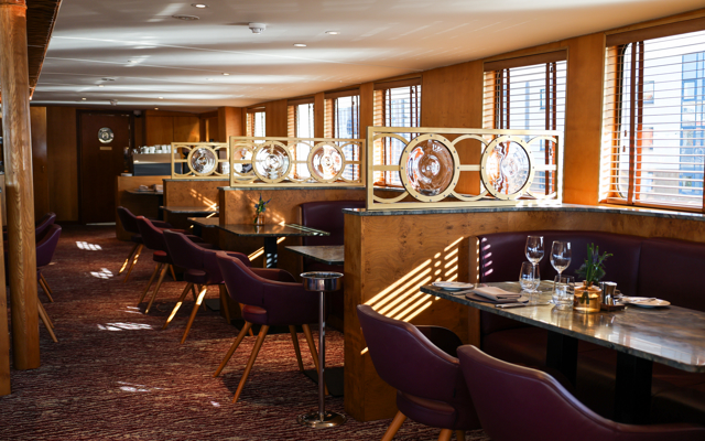 Interior shot of The Lighthouse restaurant aboard Fingal, an iconic floating hotel in Edinburgh, showcasing elegant tables set for fine dining with warm wood interiors, plush seating, and natural light streaming through the windows.
