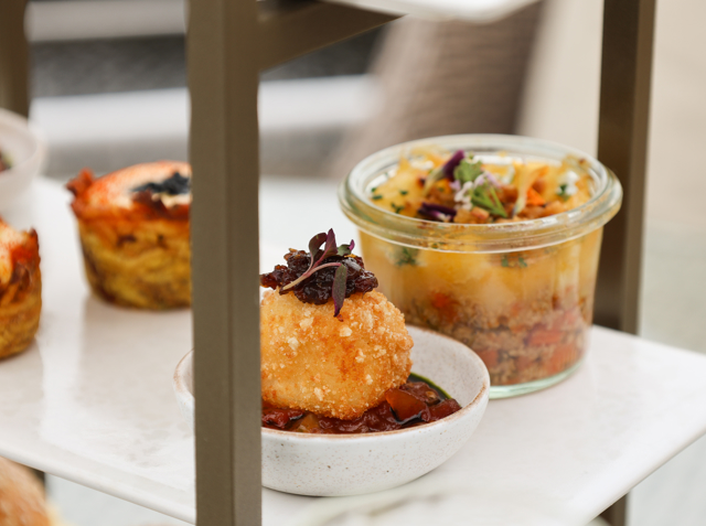 Marble tray with a savoury jar, baked bites, and a plated croquette in sauce.